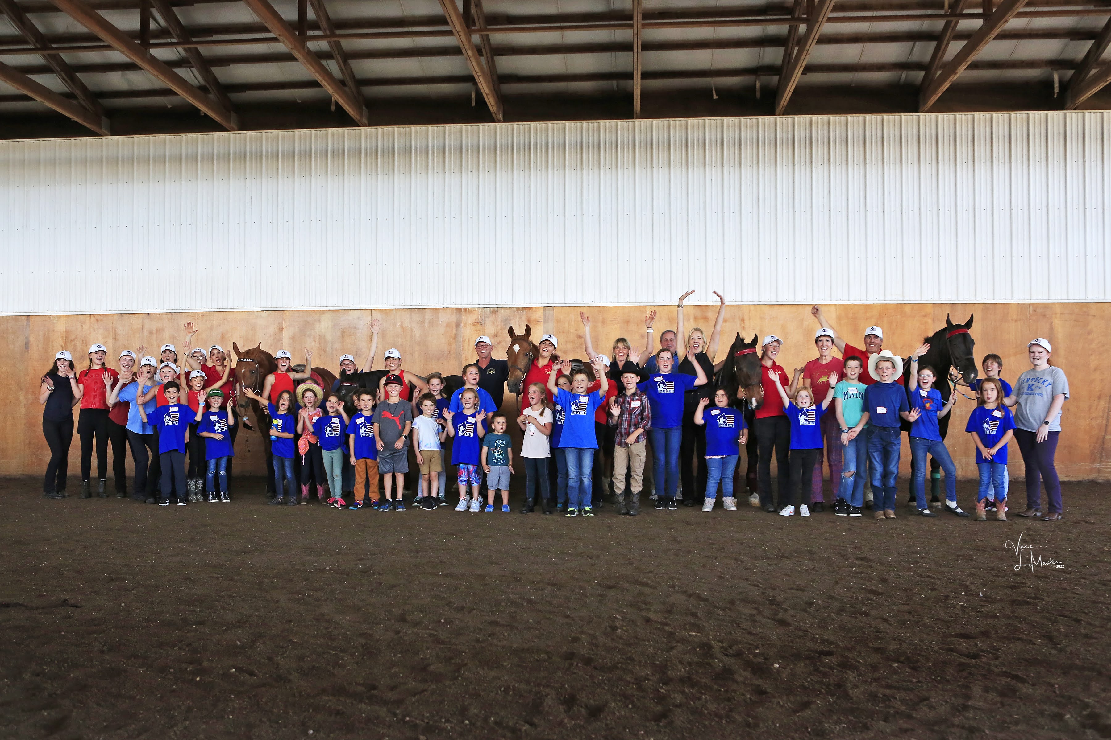 Many equine enthusiasts of all ages posing in a barn.